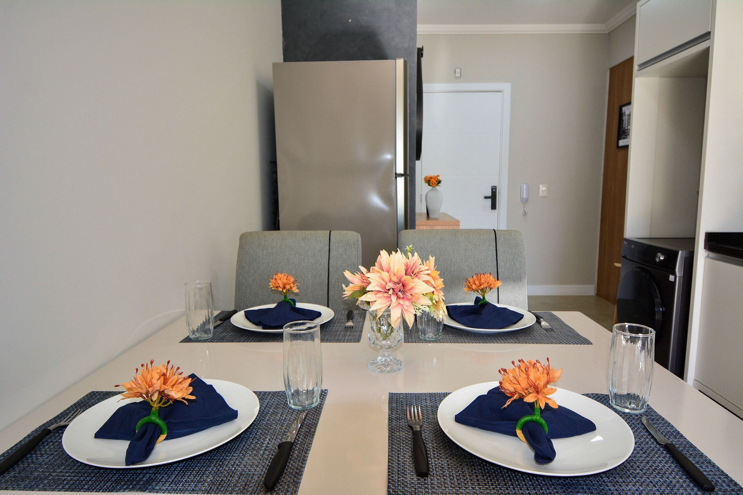 Una mesa de comedor dispuesta con platos, servilletas, cubiertos y centros de mesa con flores.