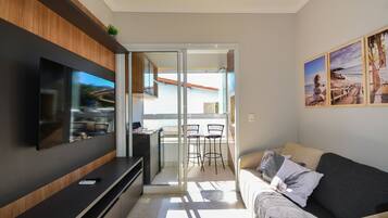 A modern living room with a flat-screen TV, a sofa, and a balcony with a dining area.