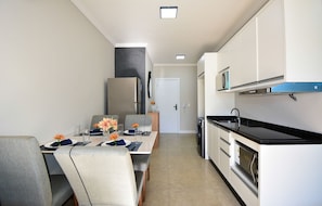 Una cocina moderna con armarios blancos, encimera negra y un comedor con una mesa lista para dos.
