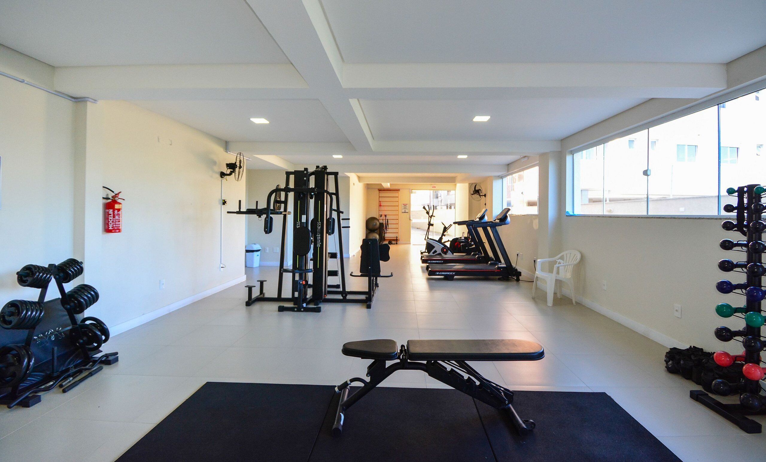 Un gimnasio con equipo de ejercicio, una banca y un extintor.