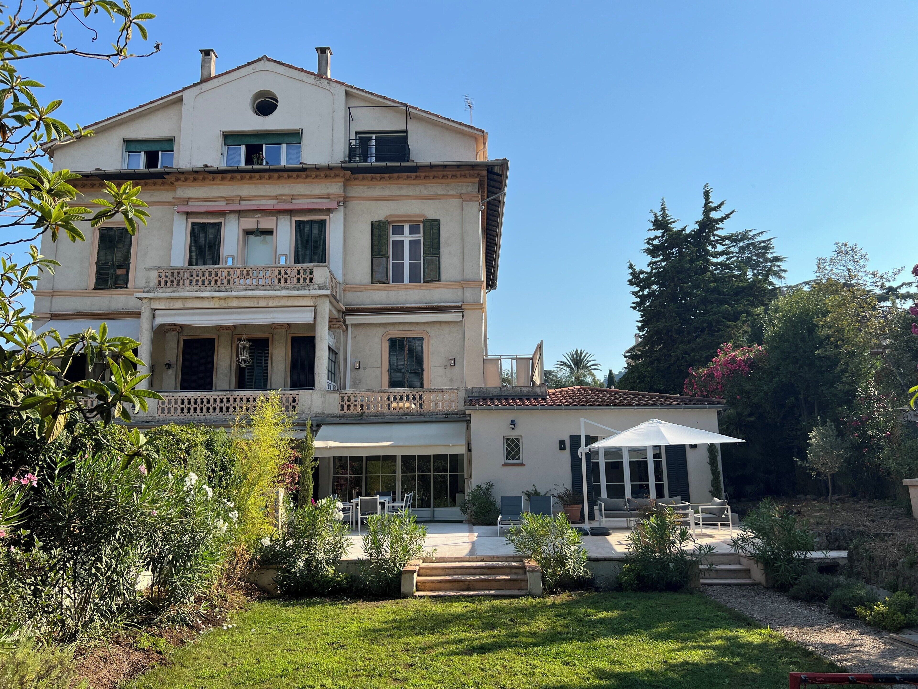 A two-story building with a balcony, a covered patio area, and a garden with various plants.