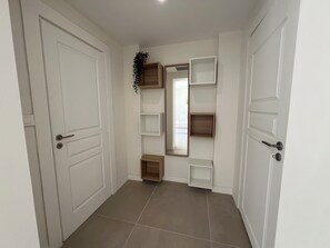 Un couloir avec des portes blanches, un sol carrelé et des étagères encastrées.