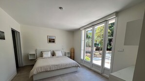Ein Schlafzimmer mit einem großen Bett, einem Nachttisch, einem Bild an der Wand und einer Glastür zum Außenbereich.