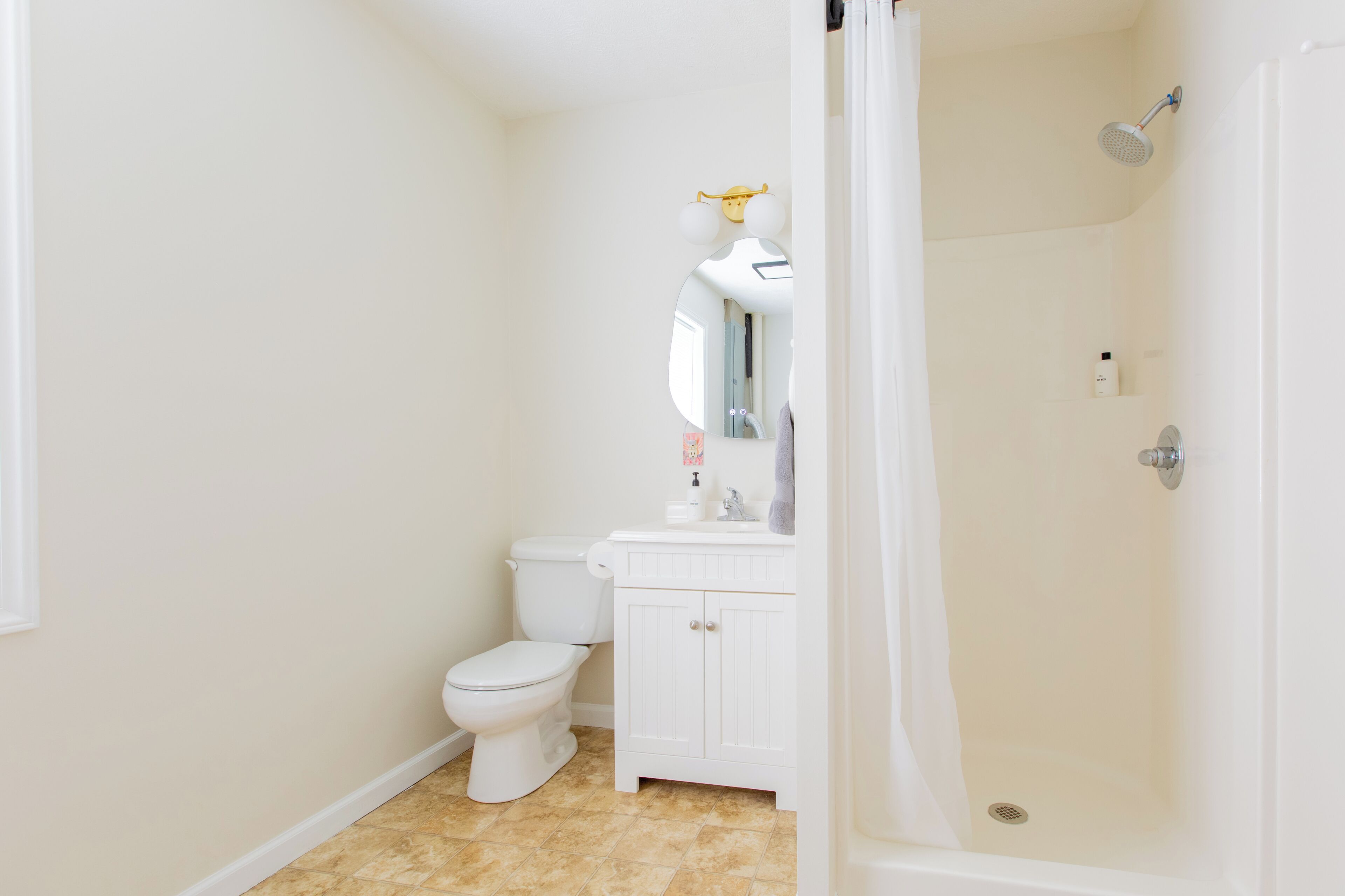 A bathroom with a toilet, sink, mirror, and shower.