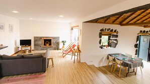 A living room with a fireplace, a sofa, a dining table with chairs, and a stone wall. - Casa da Petra – Our Casa is your Casa (Urzelina)