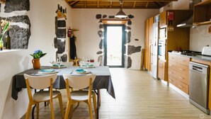 A rustic kitchen with wooden cabinets, a stove, and a dining area with a table set for four. - Casa da Petra – Our Casa is your Casa (Urzelina)