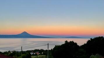 A coastal landscape with a mountain in the distance, a calm body of water, and residential buildings with red roofs.