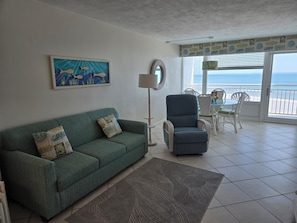 A living room with a green sofa, a blue armchair, a round table with chairs, a floor lamp, and a painting of fish. - Oceanfront Balcony - Pool - Islander Beach Resort, New Smyrna Beach! (New Smyrna Beach)