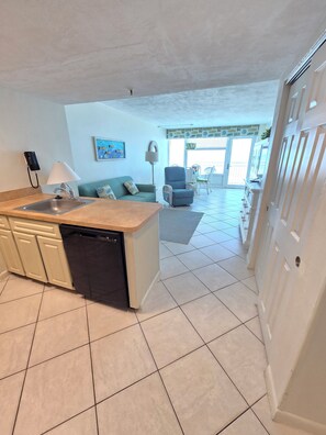 A kitchen with a dishwasher, a sink, and a telephone. There is a dining area with a table and chairs.