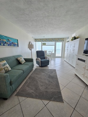 A living room with a green sofa, a blue armchair, a white cabinet, and a television. - Oceanfront Balcony - Pool - Islander Beach Resort, New Smyrna Beach! (New Smyrna Beach)