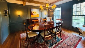 Een eetruimte met een houten tafel, stoelen, een kroonluchter en een groot raam met uitzicht.