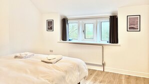 Una camera da letto con un letto, una finestra con tende, un termosifone e quadri appesi al muro.