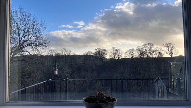 A window with a bowl on a windowsill, a railing, and a view of trees and hills. - DALE VIEW, Youlgreave, bright and cozy cottage in the heart of the Peak District (Youlgreave)