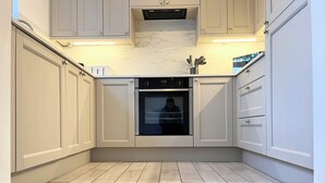 A kitchen with a built-in oven, white cabinetry, and a marble countertop. - DALE VIEW, Youlgreave, bright and cozy cottage in the heart of the Peak District (Youlgreave)