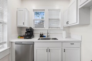 A modern kitchen with white cabinetry, a dishwasher, a coffee maker, and a window with blinds. - NEW! The River Palm-Downtown San Marco/JAX -Spa-Firepit- Pet Friendly (Jacksonville)