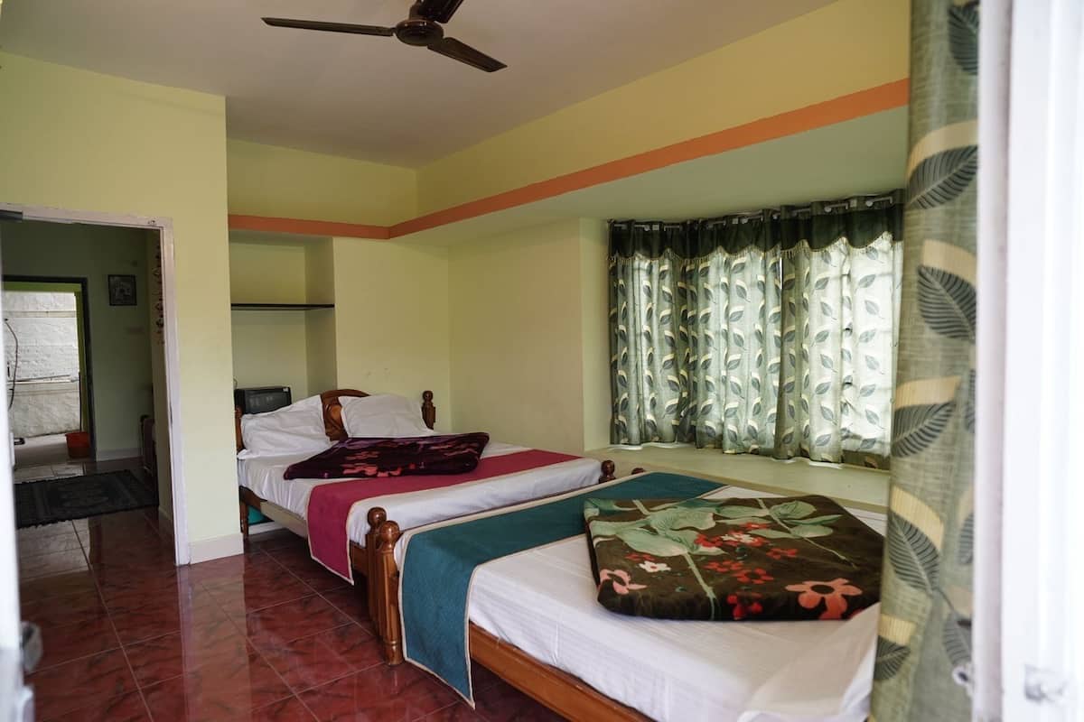 Habitación con dos camas, ventilador de techo, ventana con cortinas y puerta que da a otra habitación.