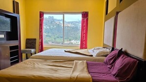 Habitación de hotel con dos camas, un televisor, una ventana y vistas a colinas, y una cortina roja.