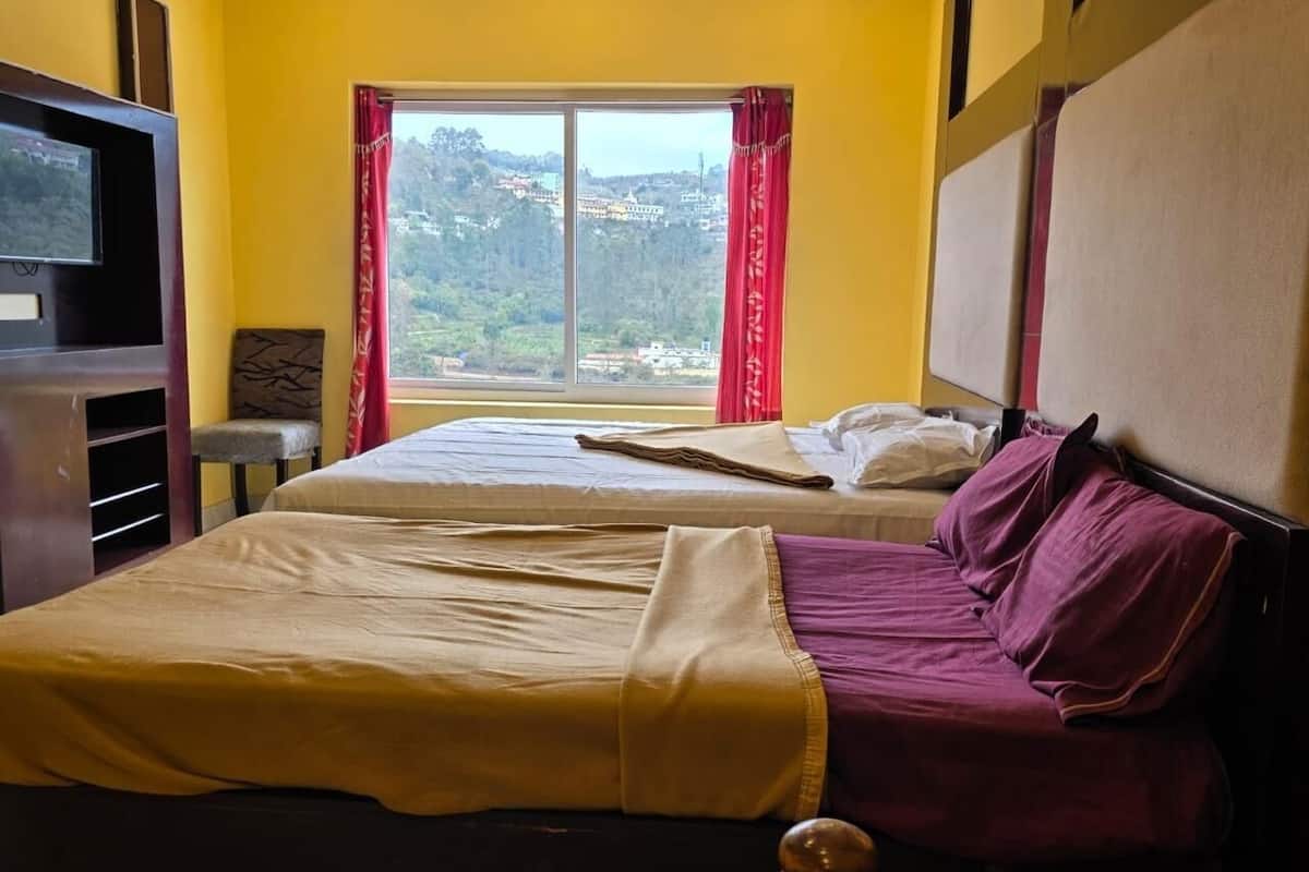 Habitación de hotel con dos camas, un televisor, una ventana y vistas a colinas, y una cortina roja.
