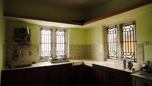 Una cocina con estufa a gas, lavamanos y dos ventanas con rejas.