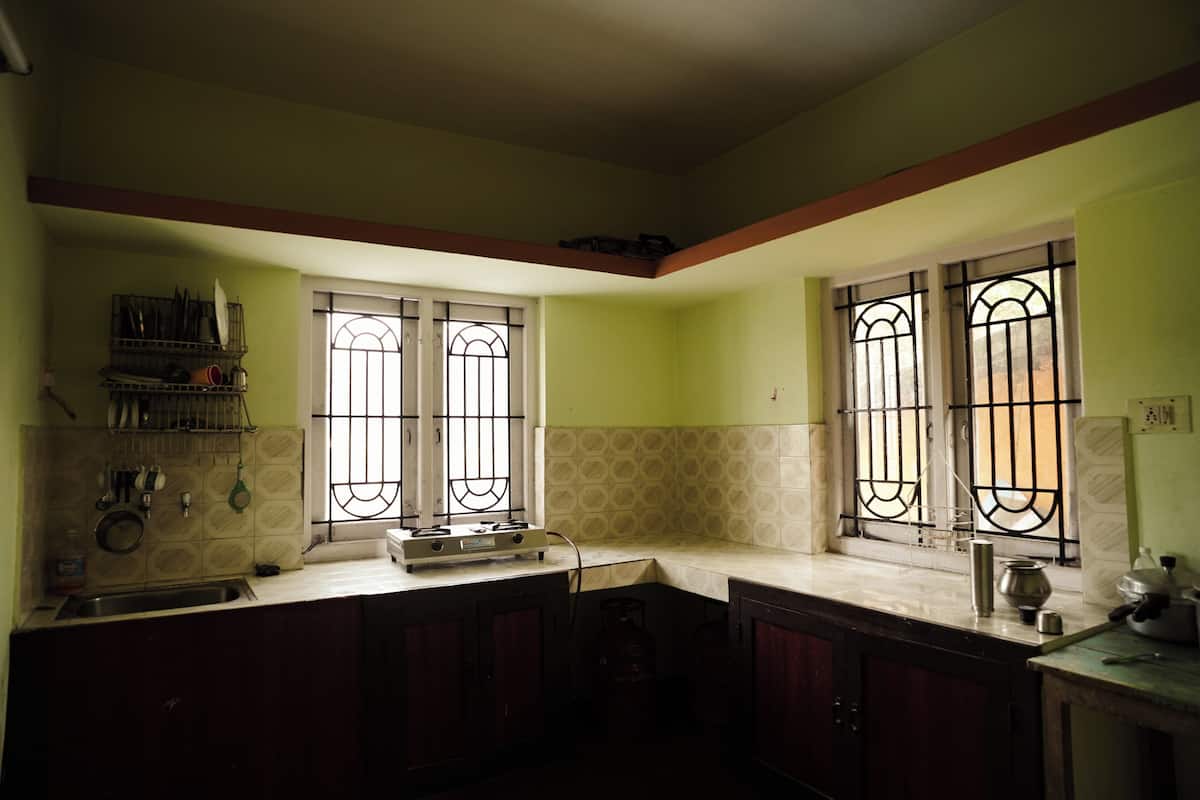 Una cocina con estufa a gas, lavamanos y dos ventanas con rejas.