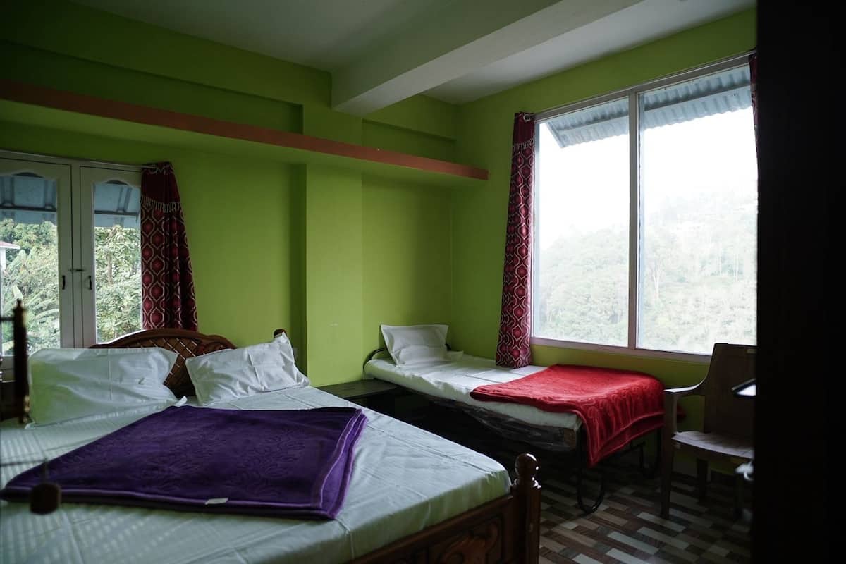 Una habitación con dos camas, una silla y una ventana que da a zonas verdes.