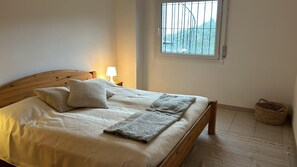 A bedroom with a wooden bed, a window with bars, a bedside lamp, and a woven basket. - 4-bedroom house with private pool in charming Begur.. (Begur)