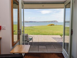 Ein Zimmer mit einer Schiebeglastür, die auf eine Terrasse mit Meerblick und eine Rasenfläche führt.