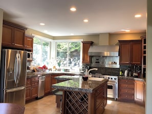 A modern kitchen with stainless steel appliances, a granite countertop, and a large window providing a view of the outdoors.