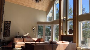 Un salón comedor amplio con techo alto, ventanas grandes y una lámpara moderna.