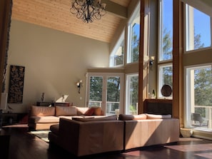 A spacious living room with a high ceiling, large windows, and a modern chandelier.