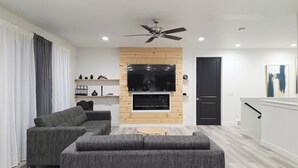 Una sala de estar moderna con un televisor de pantalla plana, sofás grises, un ventilador de techo y una pared de acento de madera.