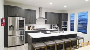 Una cocina moderna con electrodomésticos de acero inoxidable, una isla central con taburetes de bar y un amplio ventanal.