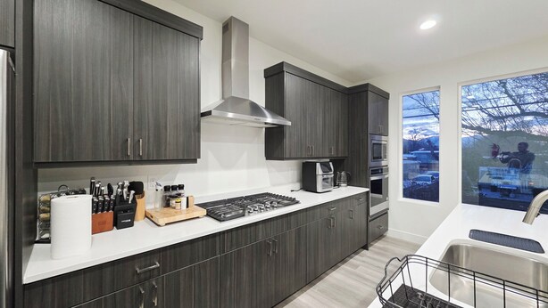 Una cocina moderna con armarios oscuros, una campana extractora de acero inoxidable y un ventanal con vistas al exterior.
