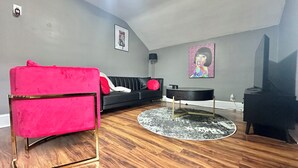 Een woonkamer met een zwarte bank, een rode fauteuil, een ronde salontafel en een zwarte tv-meubel.