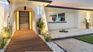 Una casa moderna con terraza de madera, entrada para coches y jardín ajardinado.