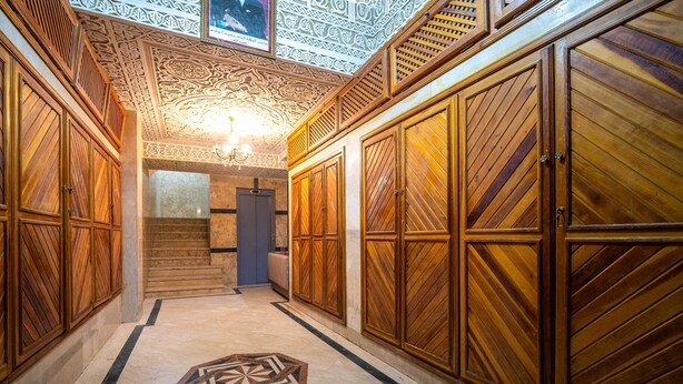 Un pasillo con paneles de madera ornamentados, un diseño geométrico en el suelo y un candelabro.