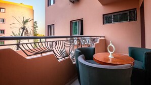 Un balcón con barandilla metálica, una mesa redonda con un jarrón y una silla color verde azulado.