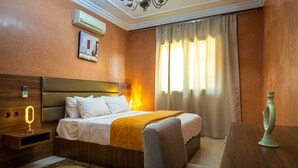 Habitación de hotel con cama, mesita de noche, lámpara y un ventanal con cortinas.