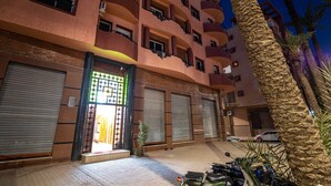 Un edificio de varios pisos con balcones, una entrada con reja y vehículos estacionados.