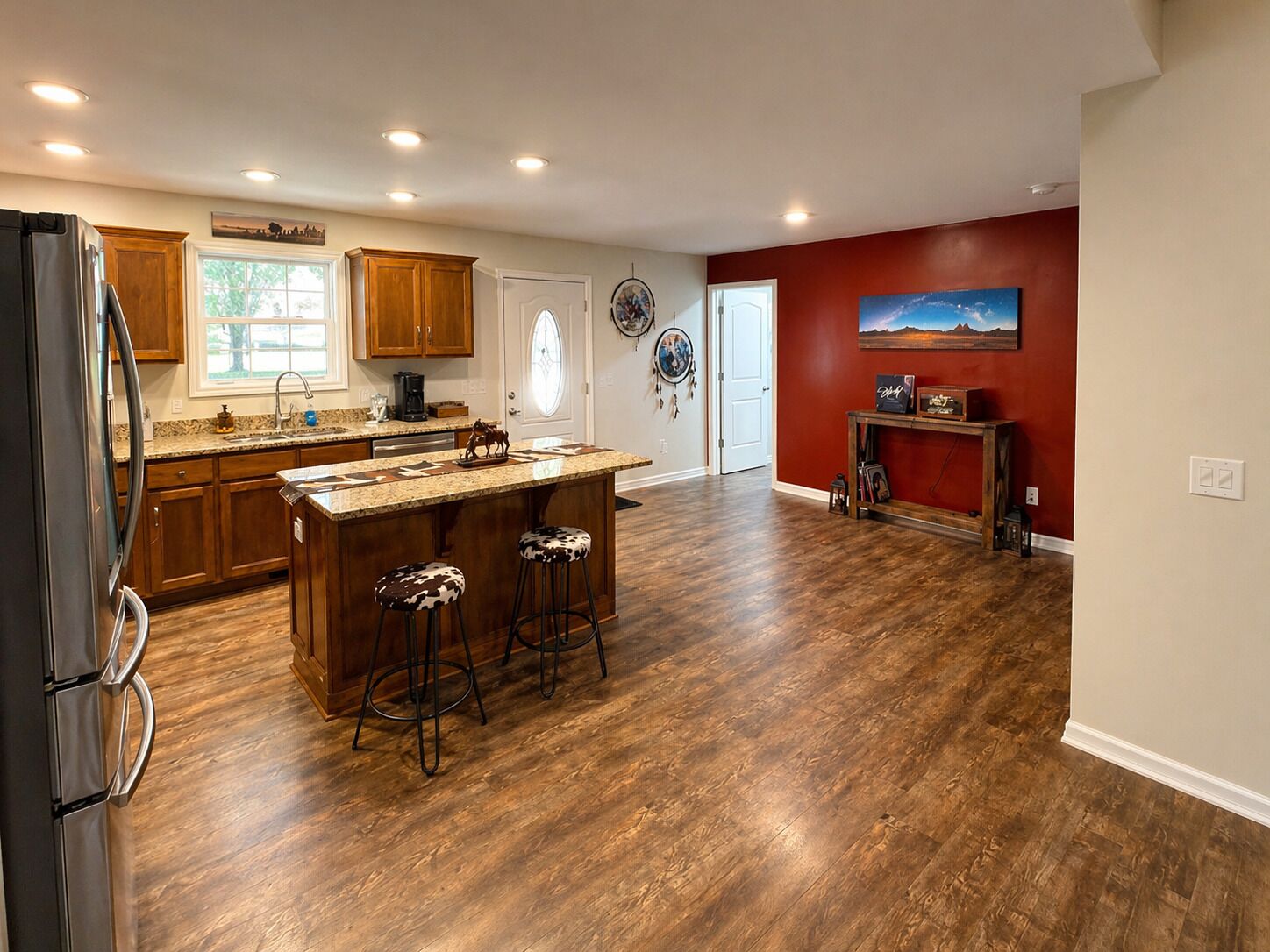 Une cuisine spacieuse avec des meubles en bois, un îlot central doté de tabourets et un mur d’accent rouge.