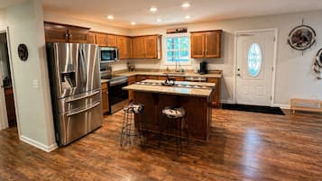 Une cuisine moderne avec des meubles en bois, des appareils en acier inoxydable, un îlot central doté de tabourets et un attrape-rêves décoratif.