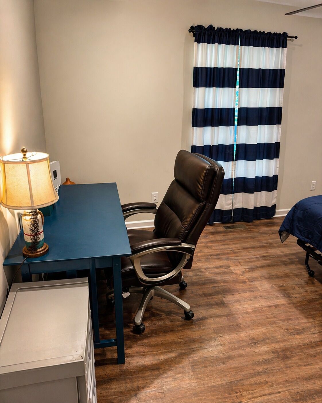 Una habitación con escritorio, silla, lámpara y ventana con cortinas a rayas.