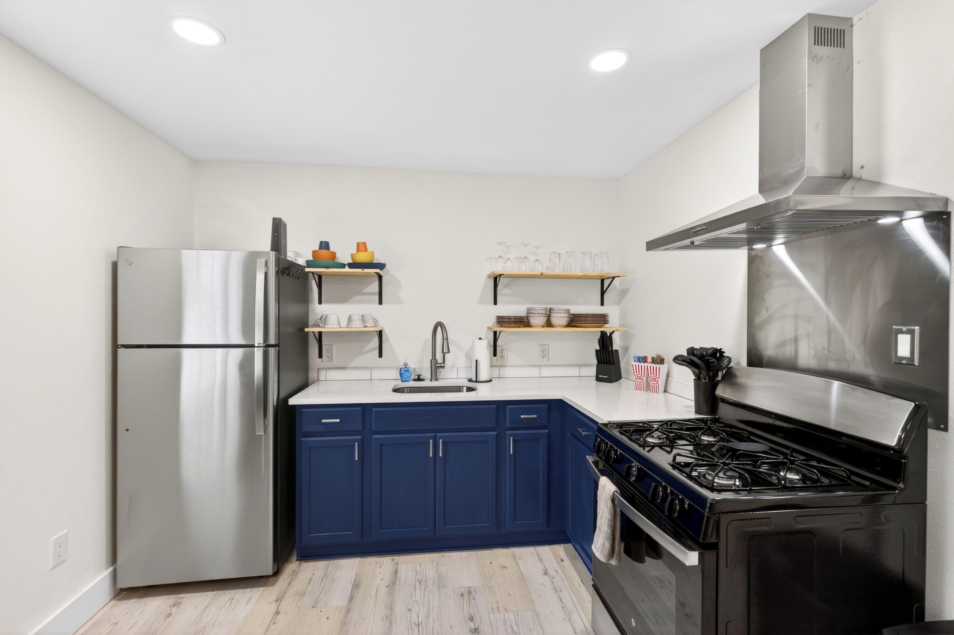 Une cuisine moderne dotée d’un réfrigérateur en acier inoxydable, de meubles bleus, d’une cuisinière à gaz et de plans de travail blancs.