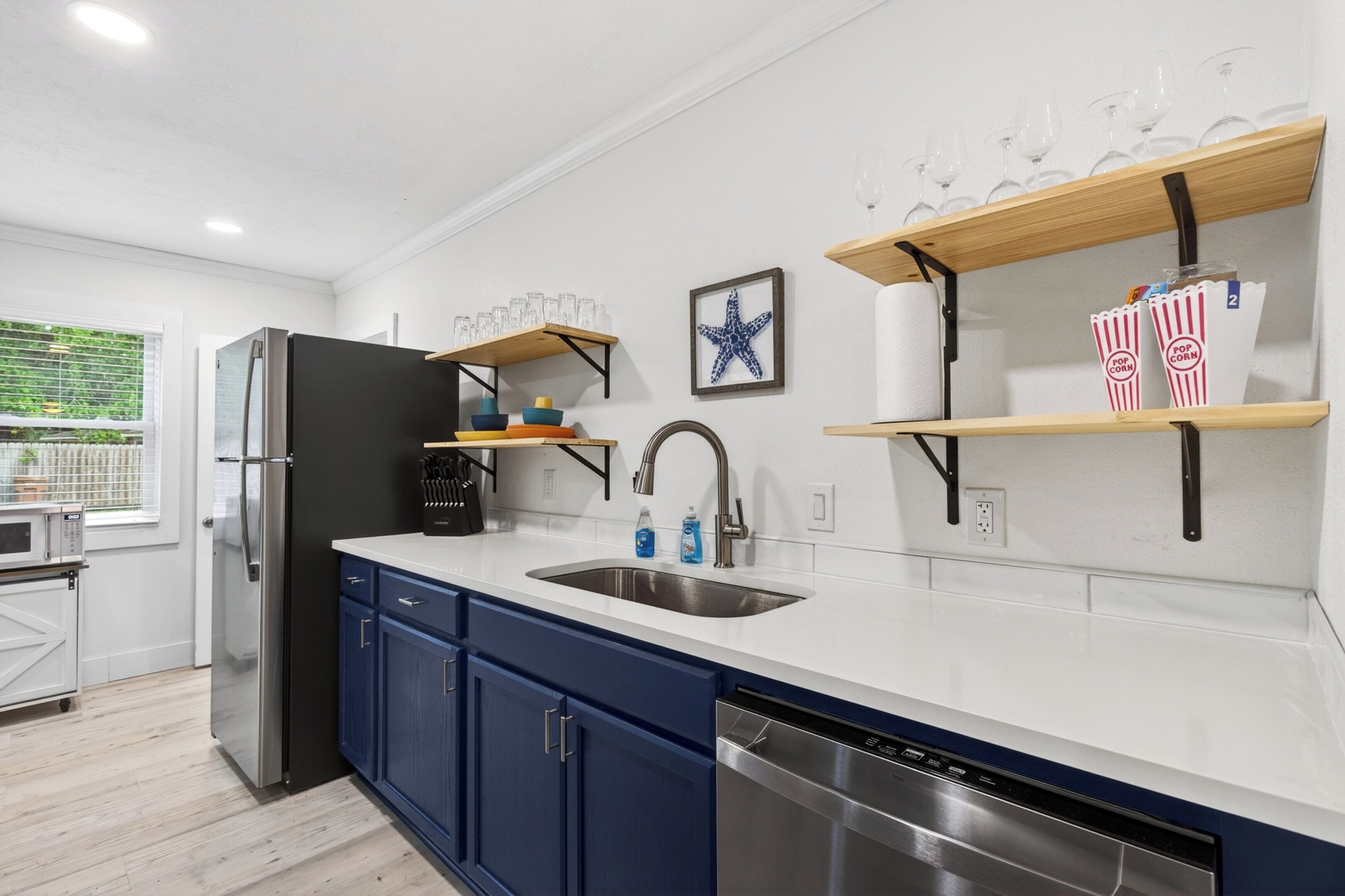 Eine moderne Küche mit einem Edelstahl-Kühlschrank, blauen Schränken, einer Spülmaschine und Holzregalen mit Gläsern und Popcorndosen.