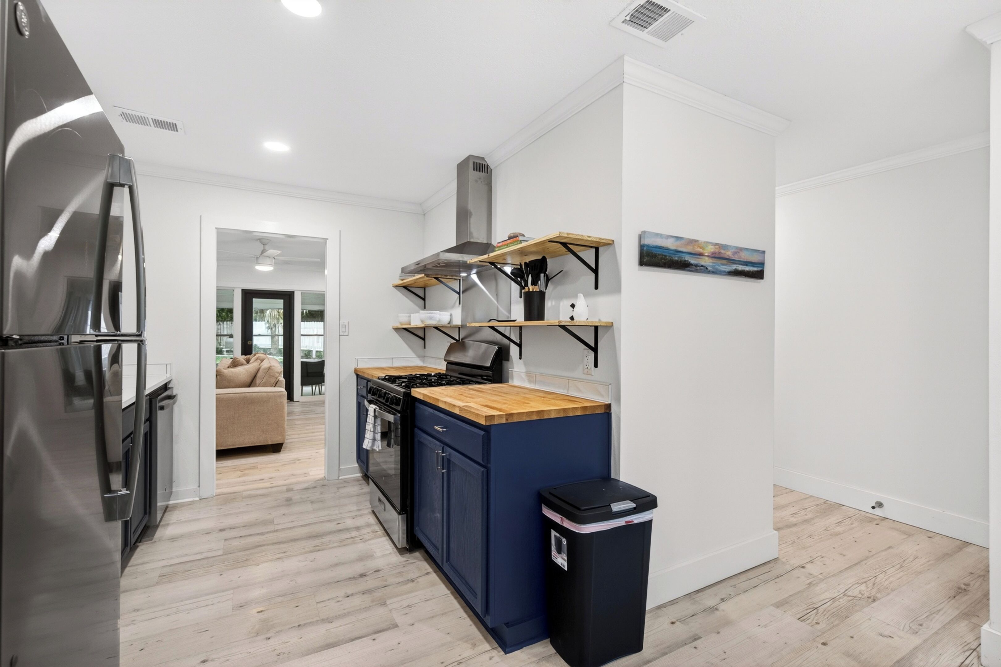 A modern kitchen with a stainless steel refrigerator, a stove, and a black trash bin.