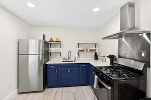 Una cocina moderna con refrigerador de acero inoxidable, gabinetes azules, estufa a gas y encimeras blancas.