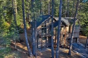 Eine Holzhütte, umgeben von hohen Kiefern, mit einer Holzterrasse und einer Treppe zum Eingang.