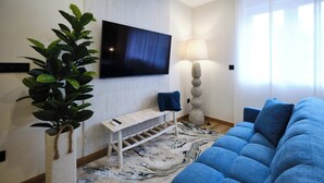 A modern living room with a flat-screen TV, a potted plant, a bench, a lamp, and a blue sofa. - Studio Premium Suite Venezia, non-smoking (Avilés)