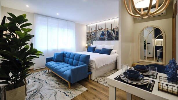 A modern bedroom with a bed, a blue sofa, a dining table with plates, and a large mirror. - Studio Premium Suite Venezia, non-smoking (Avilés)