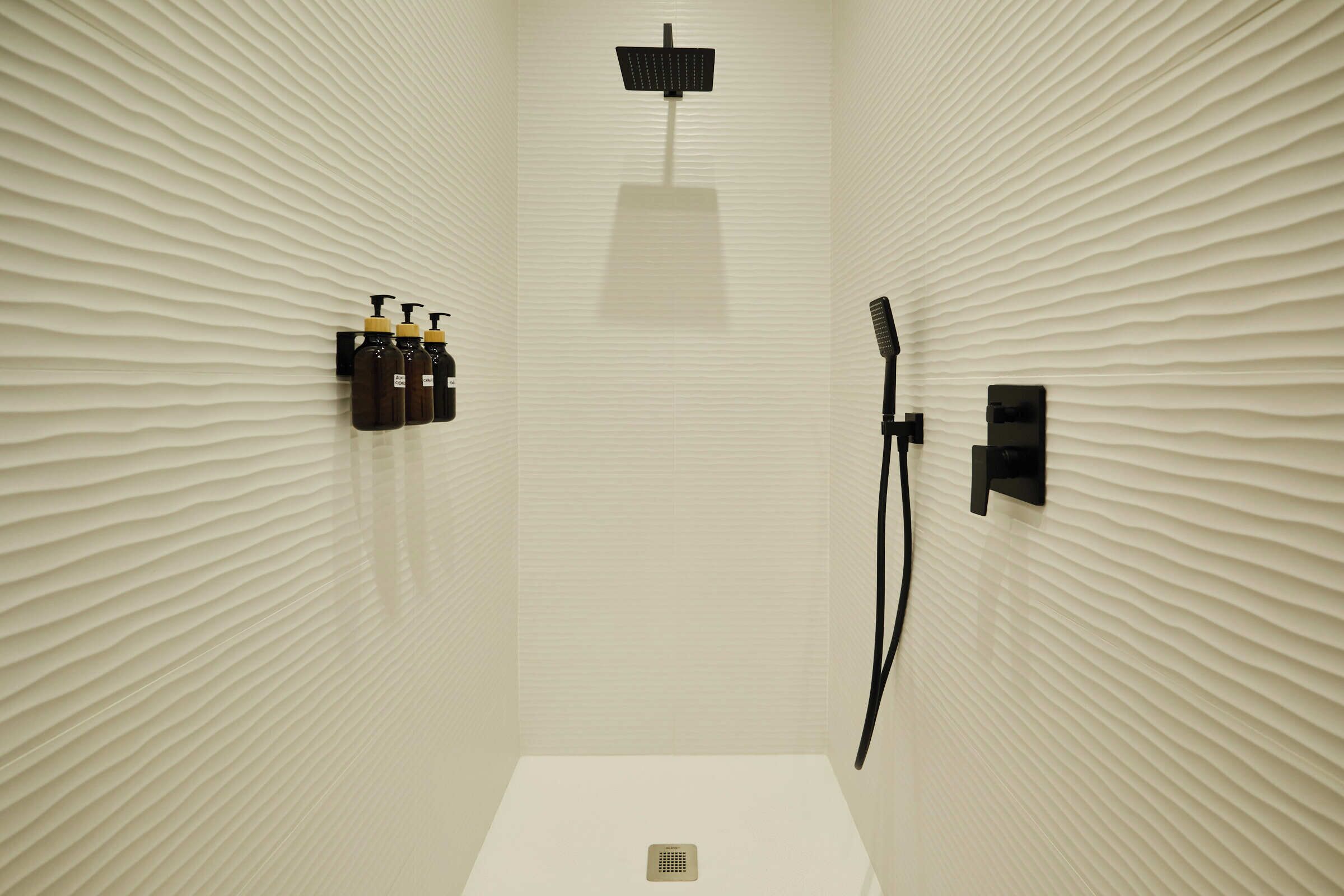 Un baño moderno con pared texturizada, un cabezal de ducha de mano, un grifo empotrado en la pared y un inodoro.